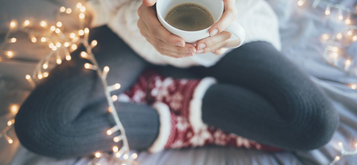 Woman sitting legs crossed on bed and holding a cup